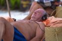 Elderly man wearing head phones sun bathing at Chaweng beach on the island of Ko Samui, Thailand.