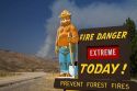 Smokey Bear extreme fire danger sign with a plume of smoke from a forest fire in the back ground in Boise County, Idaho, USA.